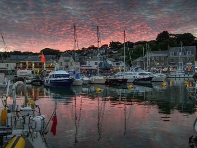 A harbor with docked boats and buildings under a colorful sky at sunset at Tides in Padstow