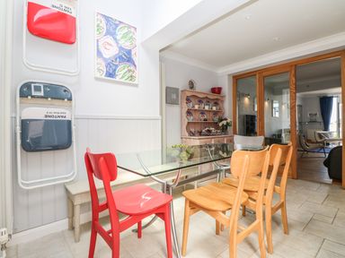 A dining area with a glass table and mixed wooden and red chairs next to a wall with folding chairs and artwork at Tides in Padstow