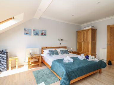 A bedroom with a wooden bed with pillows and a blue quilt with a wooden wardrobe and bedside tables at Tides in Padstow