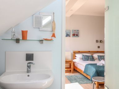 A bathroom sink with a glass shelf and small mirror above and a bedroom with a wooden bed and teal bedding at Tides in Padstow