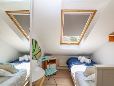 A small attic bedroom with a bed, folded towels, a blue chair, a desk, a skylight window, and a mirror on the wall at Tides in Padstow
