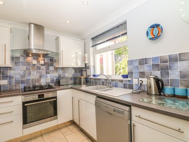 A kitchen with white cabinets a stainless steel oven and dishwasher and blue tiled backsplash at Tides in Padstow