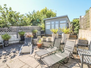 An outdoor patio area with sun loungers, potted plants, and a small shed at Tides Padstow