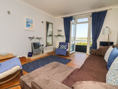 A living room with a brown sofa blue curtains and a balcony door open to a view at Tides in Padstow
