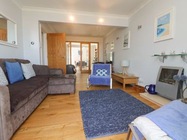 A living room with brown sofa a blue armchair a blue rug wooden floor and a wall-mounted television at Tides in Padstow