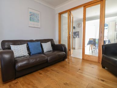 A living room with a dark brown leather sofa and three cushions near glass sliding doors at Tides in Padstow
