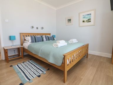 A bedroom with a wooden bed with green bedding and striped pillows next to a small wooden bedside table with a blue lamp and two framed pictures on the wall at Tides Padstow