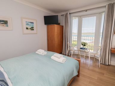 A bedroom with a bed with blue bedding and white towels a wooden wardrobe and a small seating area by a window at Tides in Padstow