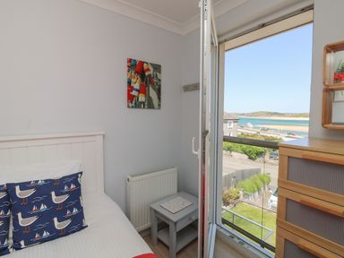 A bedroom with a bed a bedside table open door with a view of water and buildings at Tides in Padstow