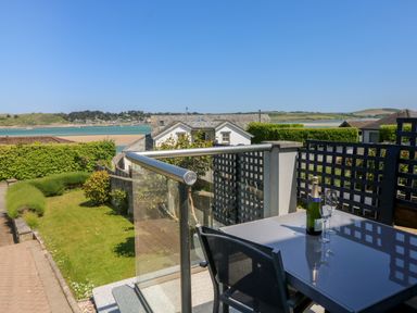 A balcony with a table and two chairs overlooking a garden and water at Tides in Padstow