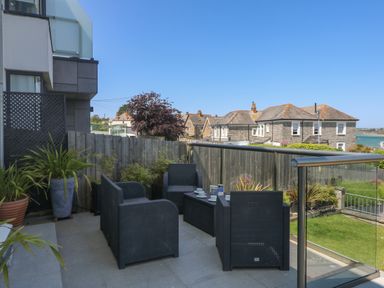 An outdoor patio with black wicker chairs a table potted plants and a view of houses and water at Tides in Padstow