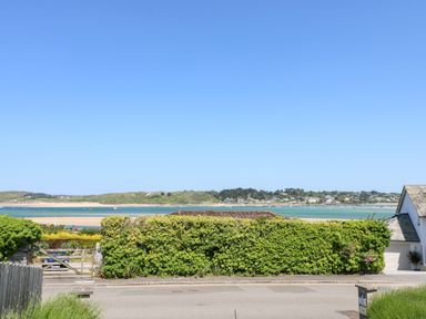 A view of water and hills across a hedge and road with a white house on the right at Tides Padstow