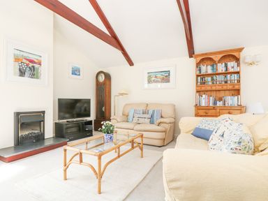 A living room with beige sofas glass coffee table wooden bookcase and television at Lookout in Falmouth