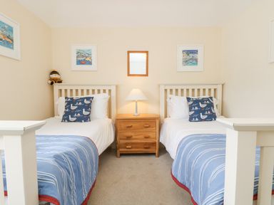 A bedroom with two single beds a wooden nightstand with a lamp and framed pictures on the walls at Lookout in Falmouth