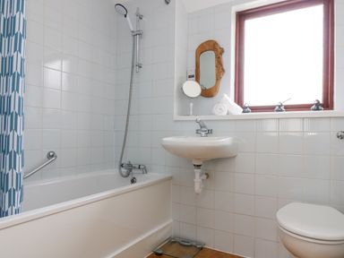 A bathroom with a bathtub shower combination a sink a toilet and a window with decorative items at Lookout in Falmouth