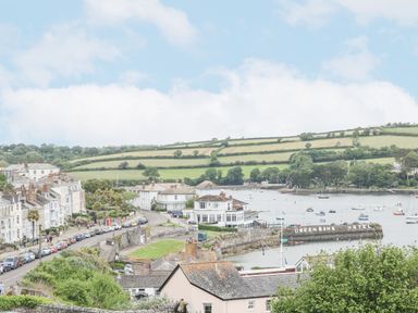 A coastal town with houses, a hotel by the water, boats in the bay, and green fields on hills at Lookout in Falmouth