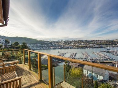 A wooden balcony with chairs overlooking a harbor with boats and houses at Totherside in Kingswear