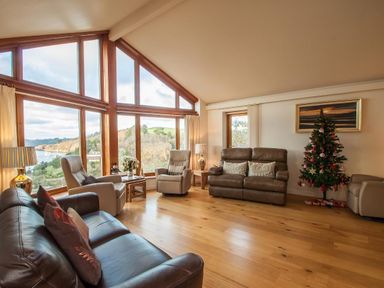 A living room with leather and fabric sofas a decorated Christmas tree and large windows showing a landscape at Totherside in Kingswear