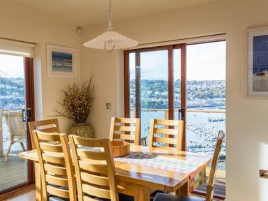 A dining room with a wooden table and chairs next to large windows overlooking a marina at Totherside in Kingswear
