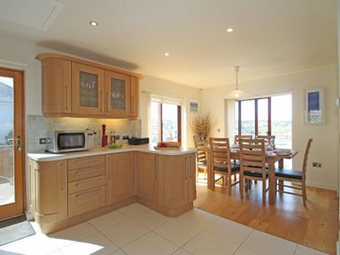 A kitchen with wooden cabinets a microwave and a dining area with a wooden table and chairs at Totherside in Kingswear