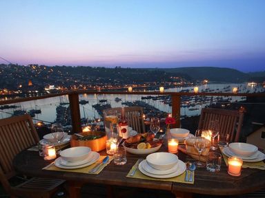 An outdoor dining table set with plates bowls glasses and candles overlooking a marina with boats at Totherside in Kingswear