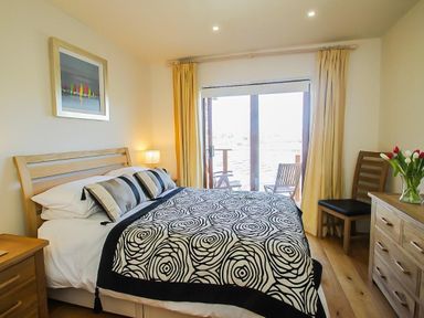 A bedroom with a double bed cushions a bedside lamp a dresser and two chairs by a sliding glass door at Totherside in Kingswear
