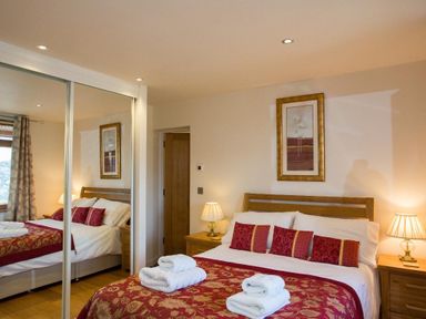 A bedroom with a double bed red and gold bedding and pillows bedside tables with lamps and a mirrored wardrobe at Totherside in Kingswear