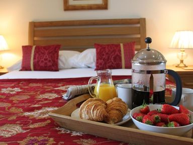 A bed with red pillows and a red patterned bedspread with a tray holding croissants coffee juice and strawberries at Totherside in Kingswear
