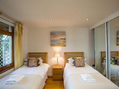 A bedroom with two single beds a bedside table with a lamp and a window with curtains at Totherside in Kingswear