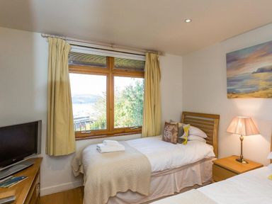 A bedroom with two single beds a wooden nightstand and a window with yellow curtains at Totherside in Kingswear
