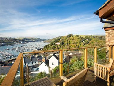 A balcony with wooden chairs overlooking a marina and hillside at Totherside in Kingswear