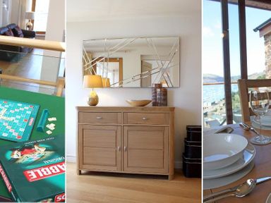 A Scrabble board game set on a table a wooden sideboard with a lamp and decorative items and a dining table set with plates glasses and cutlery with a view of water at Totherside in Kingswear