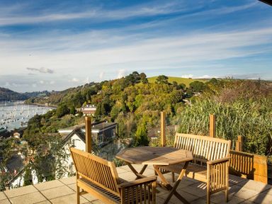 An outdoor patio with wooden benches and a table overlooking a hillside and a body of water at Totherside in Kingswear