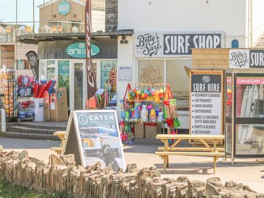A surf shop with surfboards and beach toys outside next to a seafood bar and grill at Seaport Lodge in Mawgan Porth