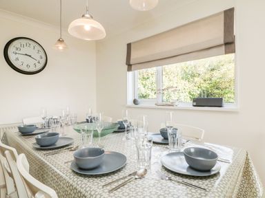 A dining room with a table set with plates bowls and glasses a large window and a clock on the wall at Seaport Lodge in Mawgan Porth