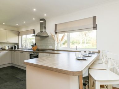 A kitchen with an L-shaped counter stools plates and cups near windows at Seaport Lodge in Mawgan Porth