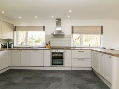 A kitchen with white cabinets two windows oven and stovetop at Seaport Lodge in Mawgan Porth