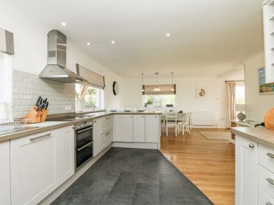 A kitchen with white cabinets and a dining area with a table and chairs at Seaport Lodge in Mawgan Porth