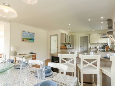 A dining table set with plates and glasses next to a kitchen with white cabinets and bar stools at Seaport Lodge in Mawgan Porth
