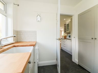 A kitchen with wooden countertops a white sink grey cabinets and a view into another kitchen at Seaport Lodge in Mawgan Porth