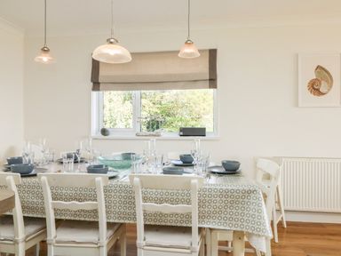 A dining room with a table set for eight under pendant lights by a window at Seaport Lodge in Mawgan Porth