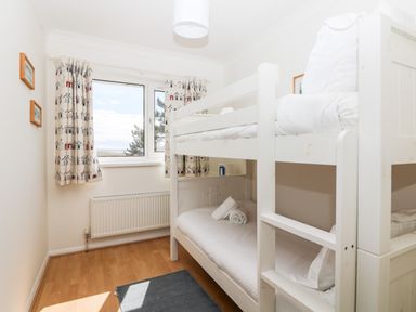 A bedroom with white bunk beds a window with patterned curtains and wooden floor at Seaport Lodge in Mawgan Porth