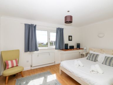 A bedroom with a bed with rolled towels a chair with a striped pillow and blue curtains at Seaport Lodge in Mawgan Porth
