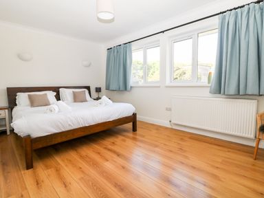 A bedroom with a wooden double bed white bedding blue curtains and wooden floor at Seaport Lodge in Mawgan Porth
