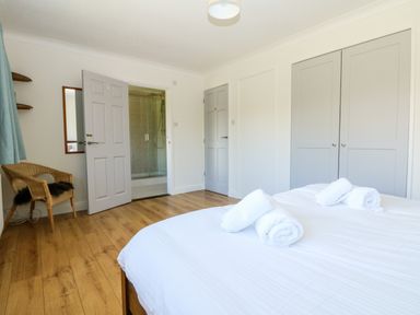 A bedroom with a bed covered in white linens and towels on top a wicker chair two gray closet doors and an open door leading to a shower at Seaport Lodge in Mawgan Porth