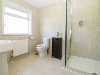 A bathroom with a toilet a wooden cabinet a shower and a window at Seaport Lodge in Mawgan Porth