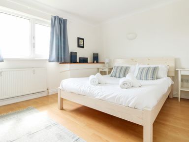 A bedroom with a double bed with striped pillows and rolled towels near a window with blue curtains at Seaport Lodge in Mawgan Porth