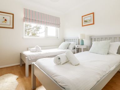 A bedroom with two single beds with white bedding and rolled towels a bedside table with a lamp and framed pictures on the walls at Seaport Lodge in Mawgan Porth