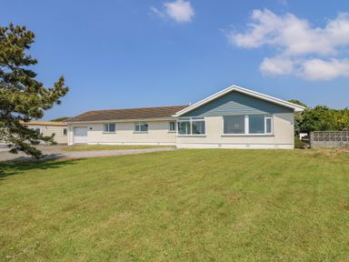 A single story house with a garage on a lawn with a paved driveway and a tree in the yard at Seaport Lodge in Mawgan Porth