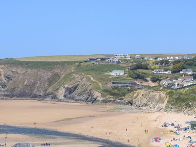A sandy beach with people and tents near rocky cliffs and houses at Seaport Lodge in Mawgan Porth